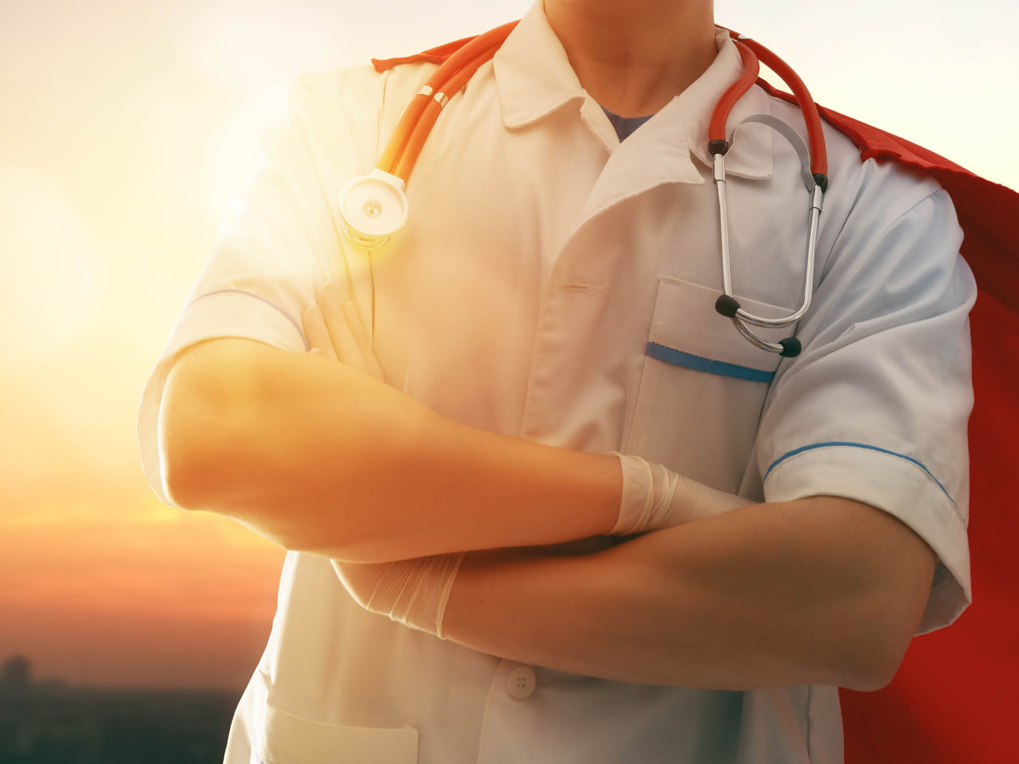 Doctor wearing facemask and superhero cape during coronavirus outbreak. Virus and illness protection, quarantine. COVID-2019. Super hero power for medicine. Person on sunset cityscape background.